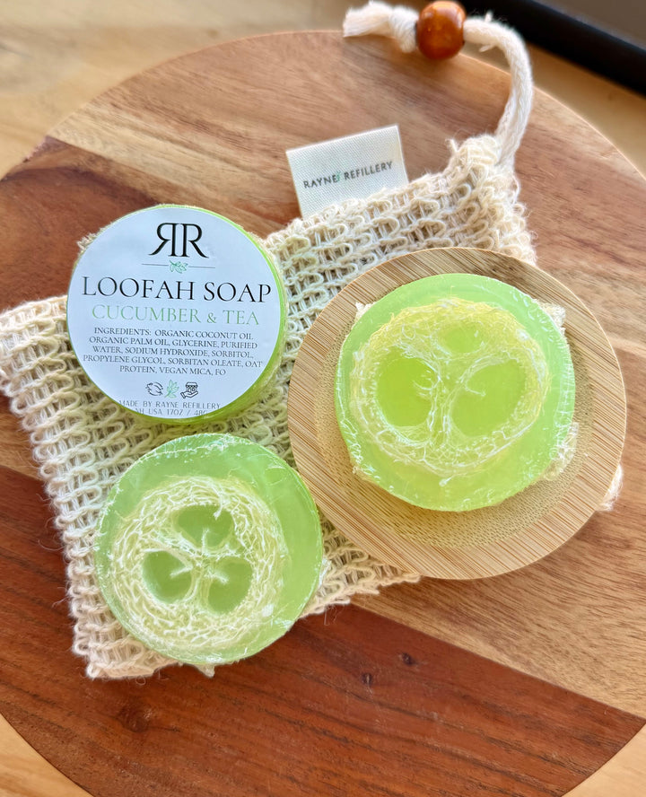 Light green loofah soap discs labeled 'Cucumber & Tea' on wooden tray with woven pouch