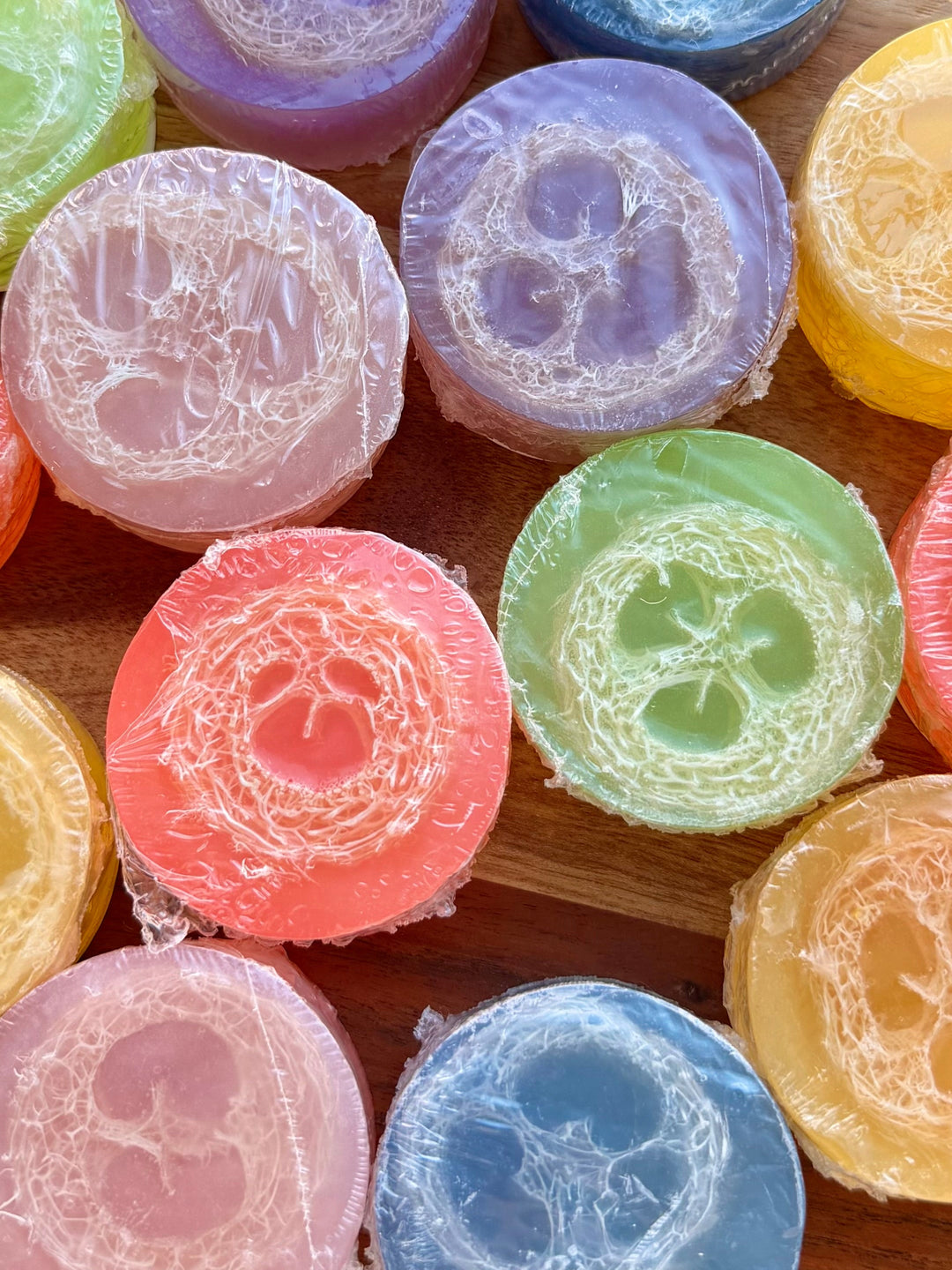 Assorted round loofah soap bars in purple, blue, pink, green, and orange with flower cores