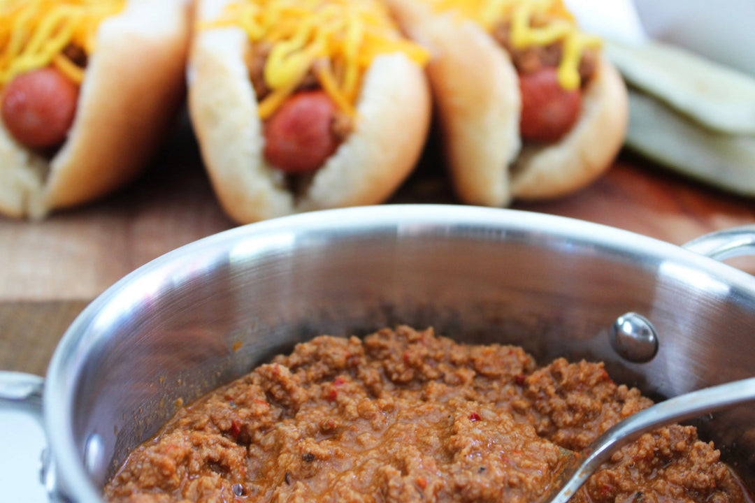 Coney Island hot dog spice blend simmering in a metal pot beside hot dog rolls