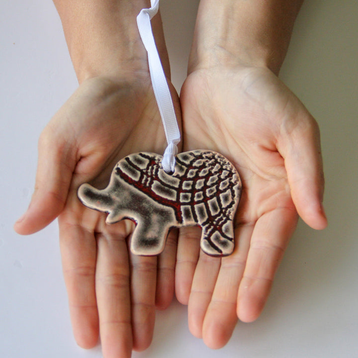 Grey patterned elephant ornament with white hanging ribbon held in two hands