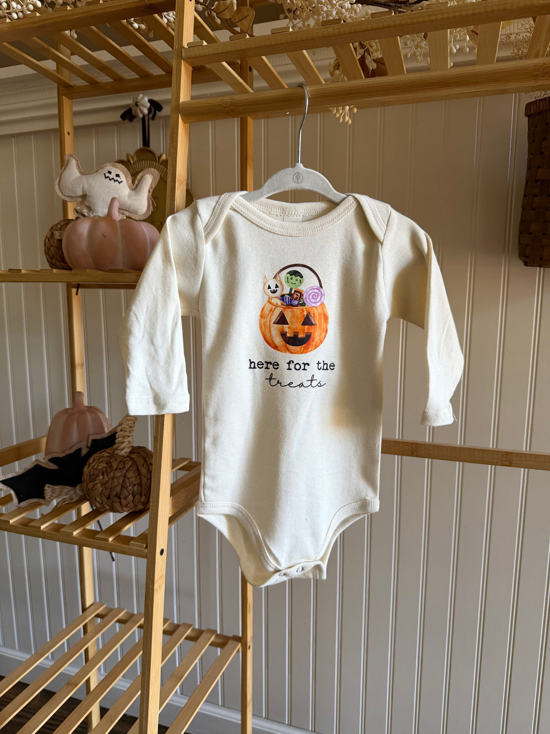 Cream long-sleeve bodysuit with front candy bucket graphic, hanging on a hanger