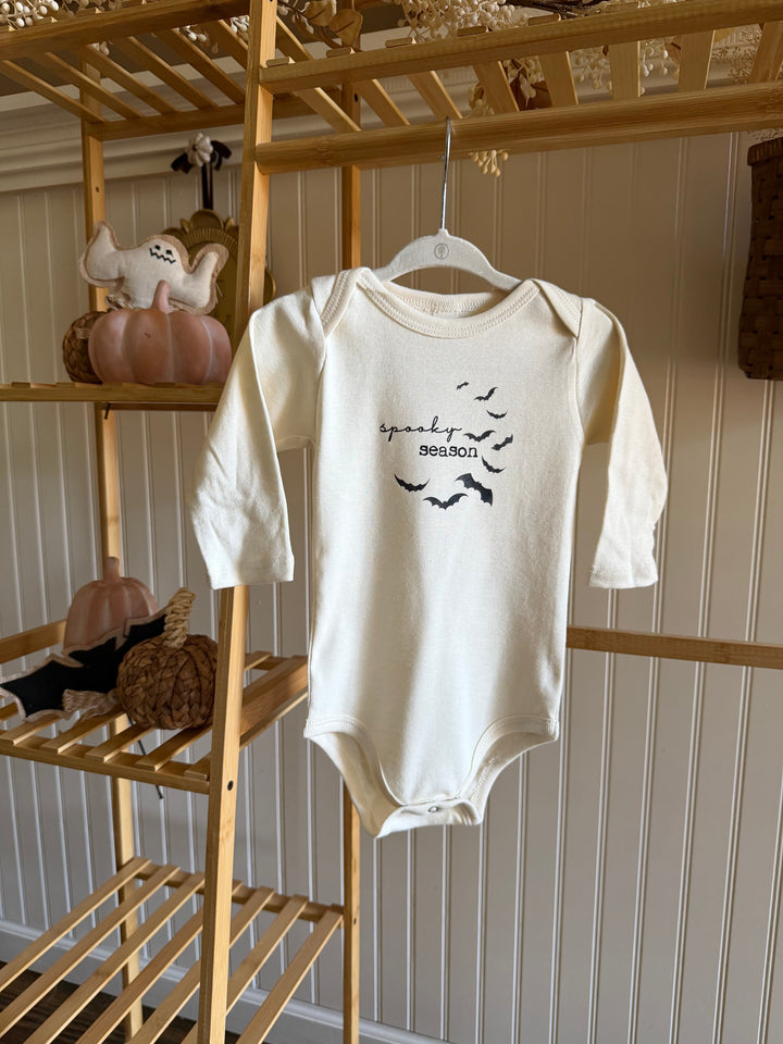 White long-sleeve bodysuit with spooky season text and bat graphic, hanging on rack