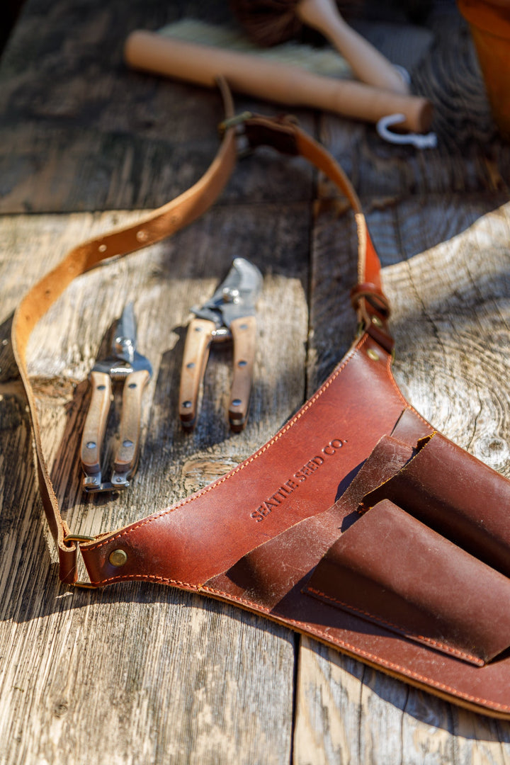 Brown leather tool belt with multiple front slots and hanging hand tools