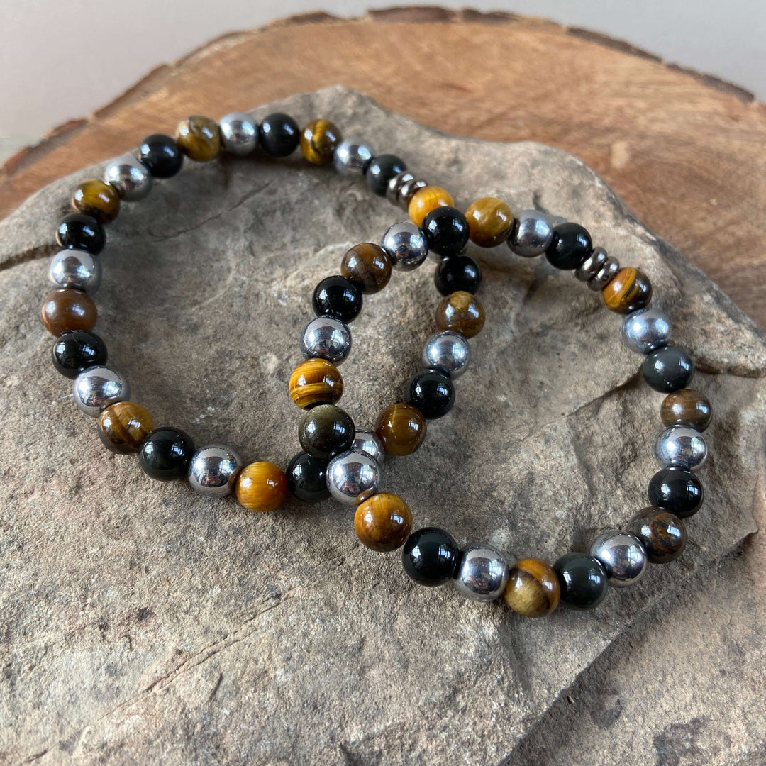 Beaded tiger eye bracelet with black beads and gold-brown stones on a stone display.