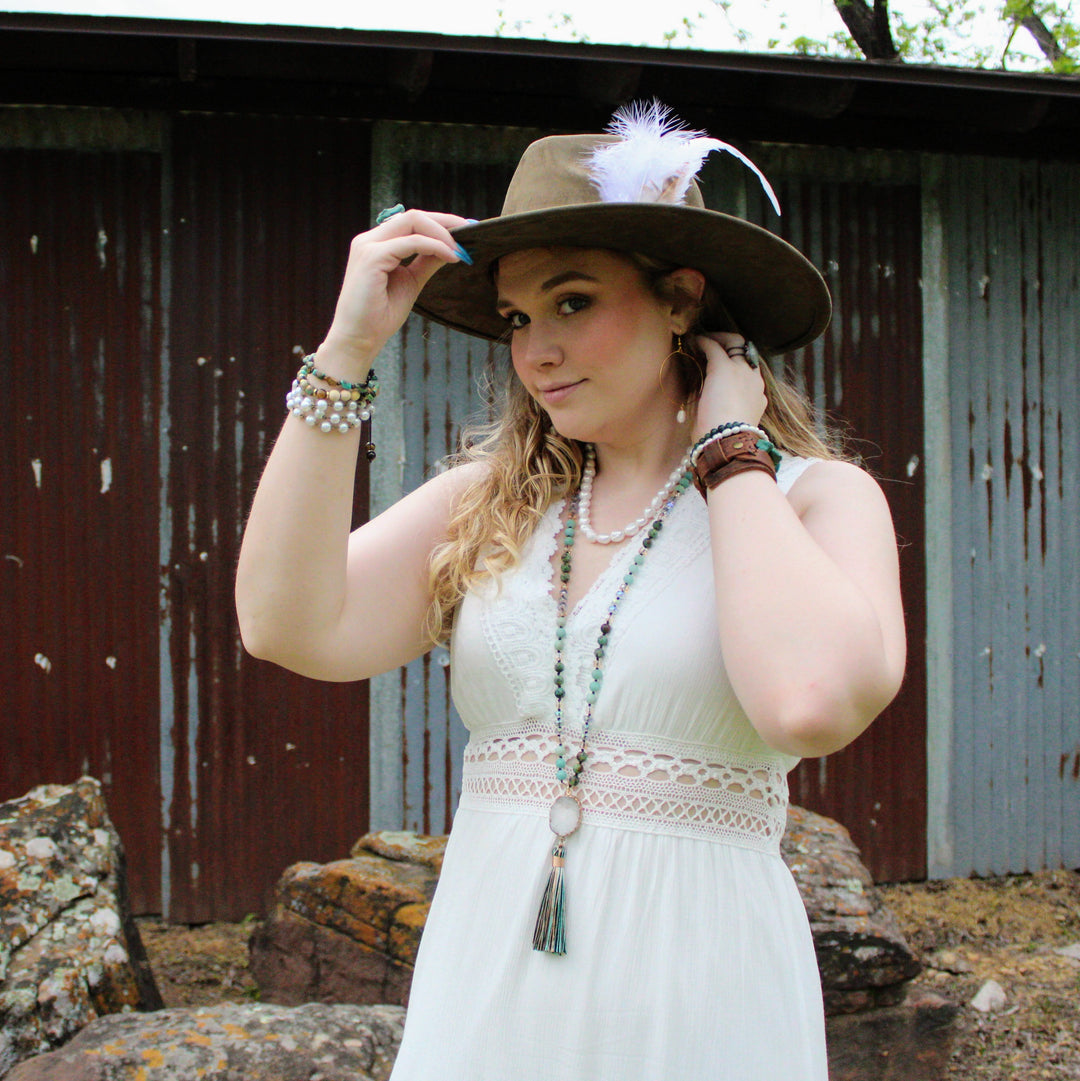 Long beaded necklace worn with white dress, featuring druzy pendant and tassel