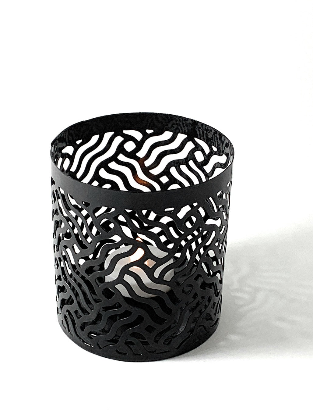 Grey metal votive candle holder with zebra-like cutout pattern, cylindrical