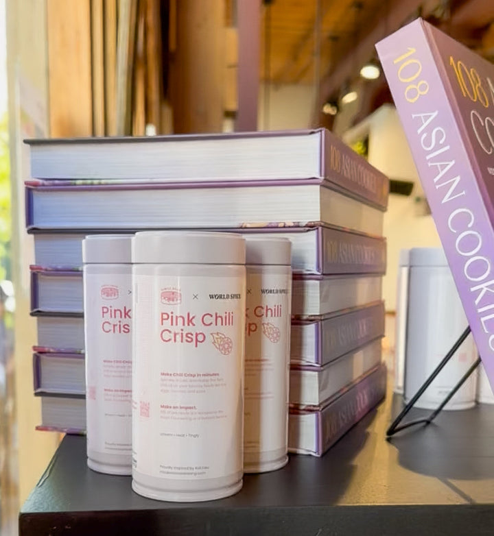 Stacked chili crisp jars with white containers and pink labels on a retail display table