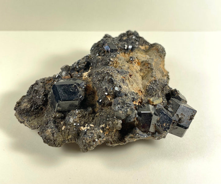 Dark crystal cluster with cube facets on dark gray rock and tan specks
