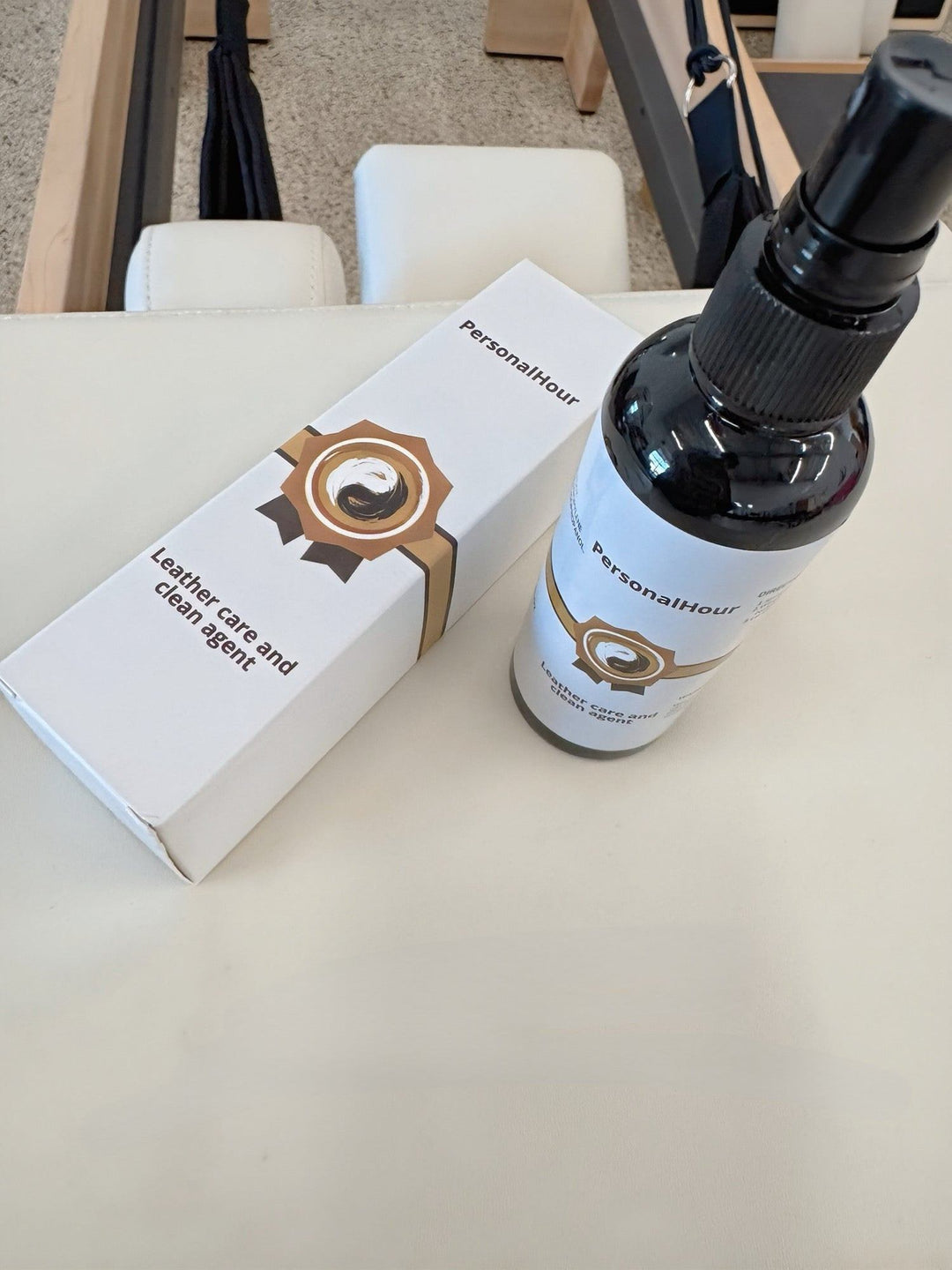 Leather care spray bottle beside closed white carton on workout bench