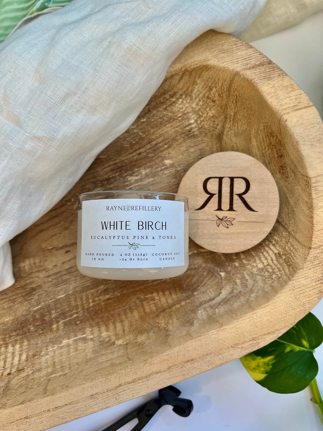 White Birch candle in white glass jar with gold lid, shown with wood coaster