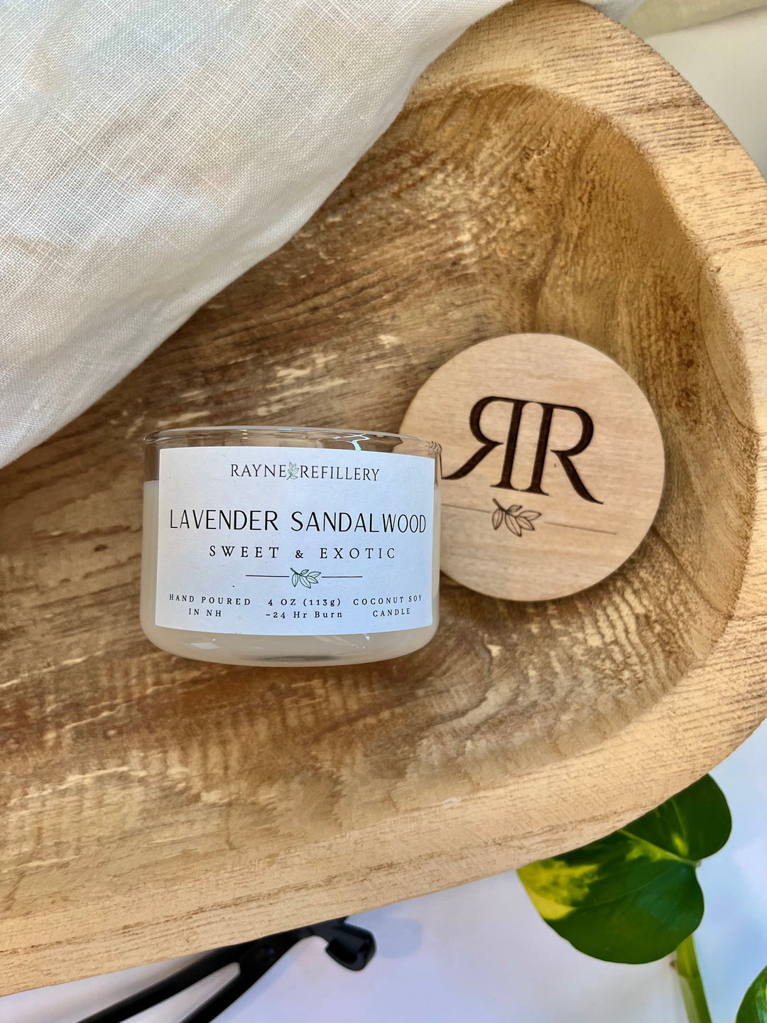 Lavender sandalwood candle in white jar with wooden lid on round wooden plate