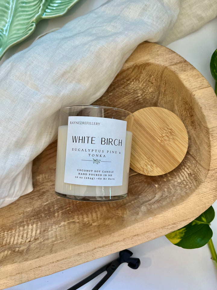 White Birch candle in white glass jar with wooden lid on oval wooden tray