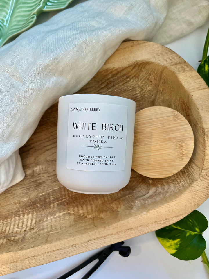 White Birch candle in white glass jar with wooden lid on oval wooden tray