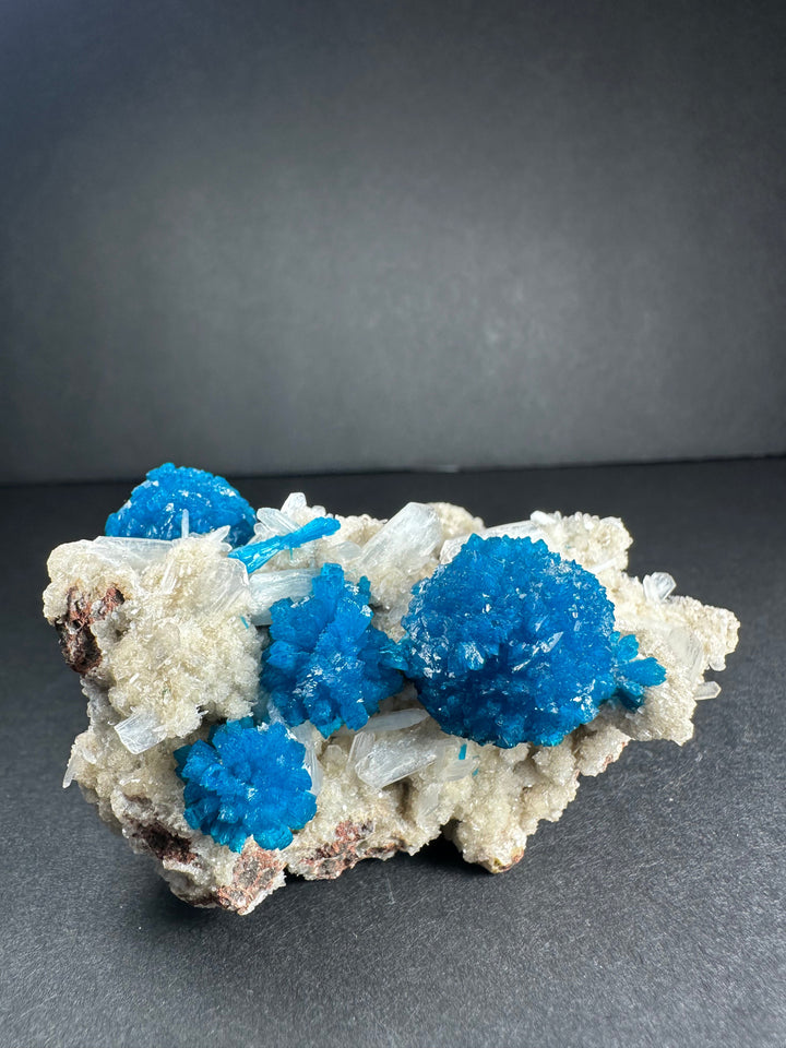 Cavansite and stilbite mineral specimen with three bright blue crystal clusters on matrix