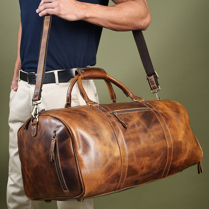 Brown leather duffel bag worn over shoulder, with adjustable strap and side pocket.