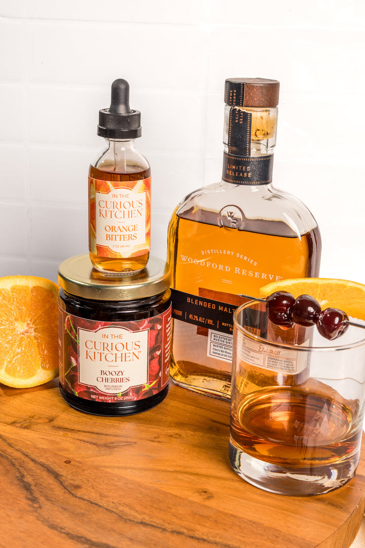 Orange bitters bottles with black droppers and amber liquid, set on wooden display with citrus.