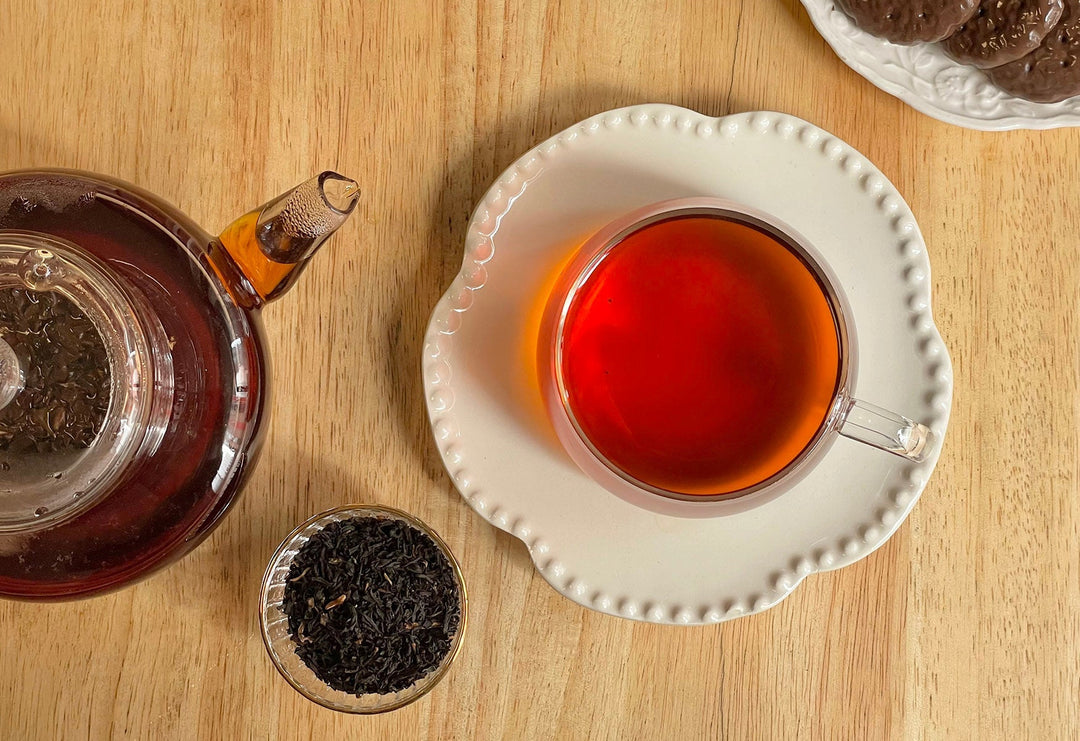 Small scoop of black tea leaves beside cup of red-brown tea