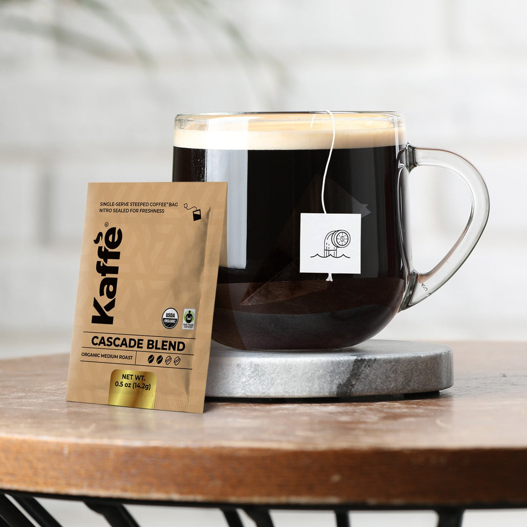 Single-serve coffee steeped bag beside glass mug with dark brewed coffee.
