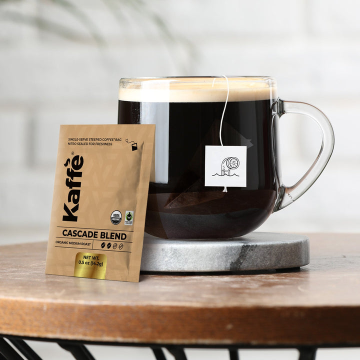 Single-serve coffee steeped bag beside glass mug with dark brewed coffee.