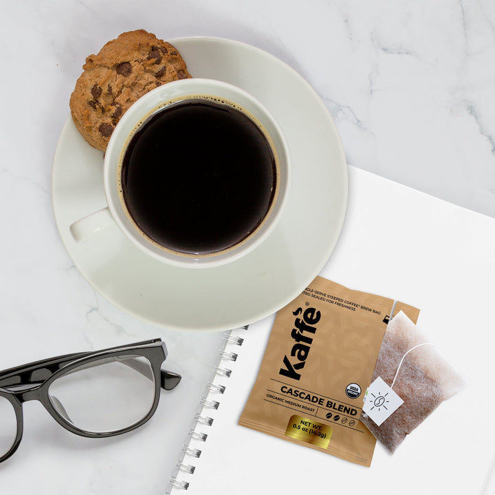Cup of dark coffee with single-serve coffee steeped bag packet on saucer.