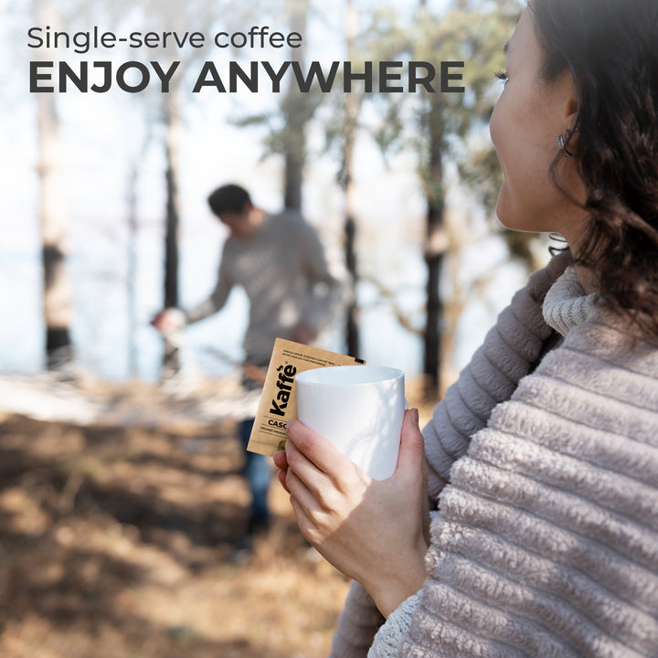 Coffee drinker holding a mug and a single-serve coffee steeped bag packet outdoors.
