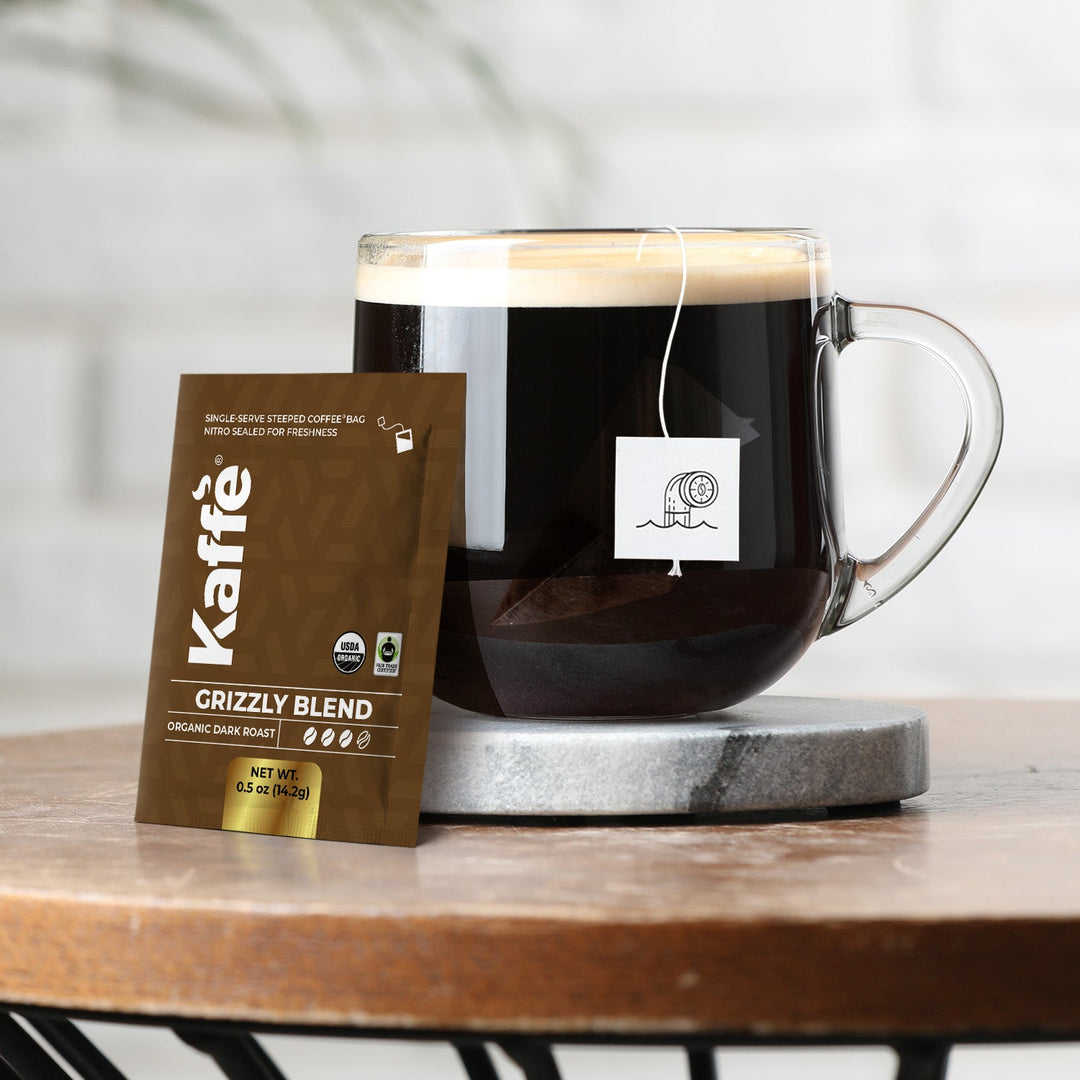 Glass mug of dark coffee with Grizzly Blend steeped bag pouch on coaster