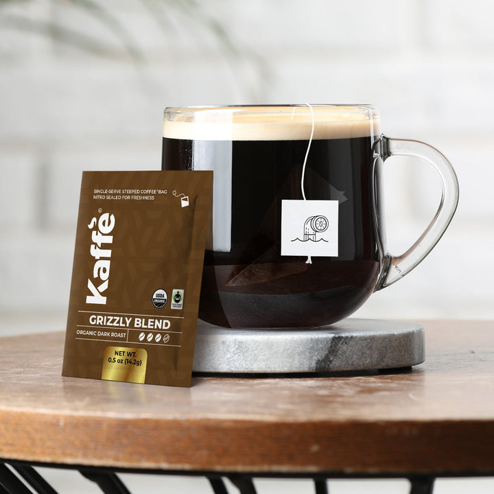 Glass mug of dark coffee with Grizzly Blend steeped bag pouch on coaster