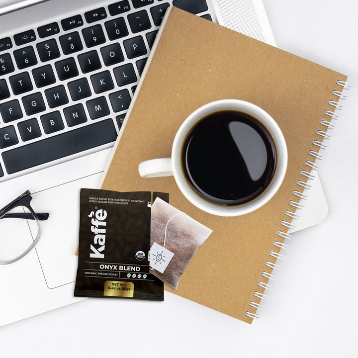 Coffee steeped bag with drawstring-style tea tag and cup of dark coffee