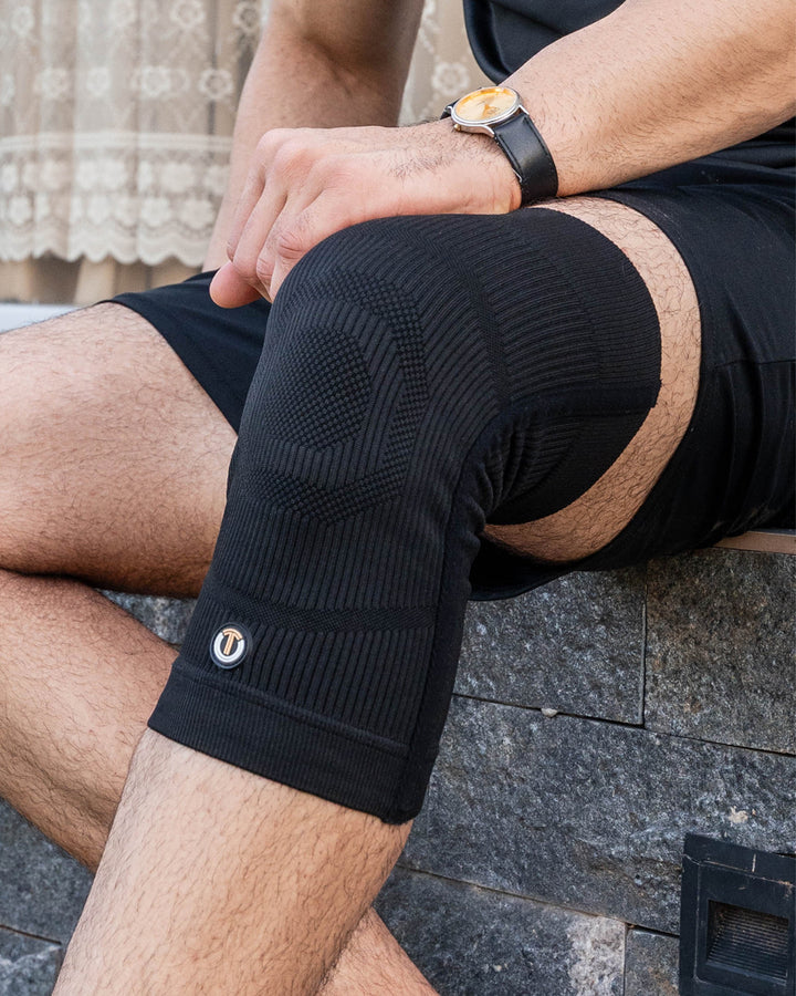 Black ribbed compression knee sleeve on leg with copper accent logo patch