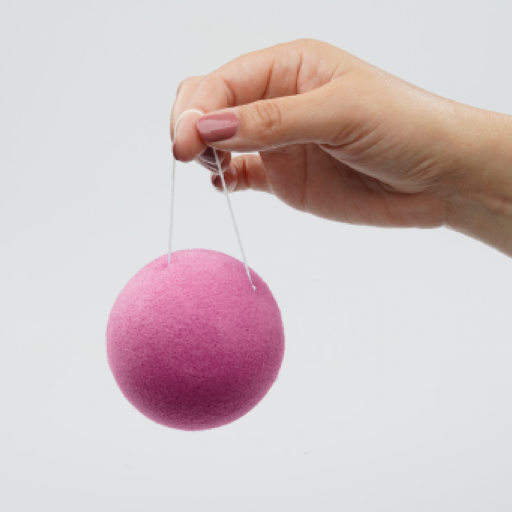 Pink konjac facial cleansing sponge suspended by a thin string