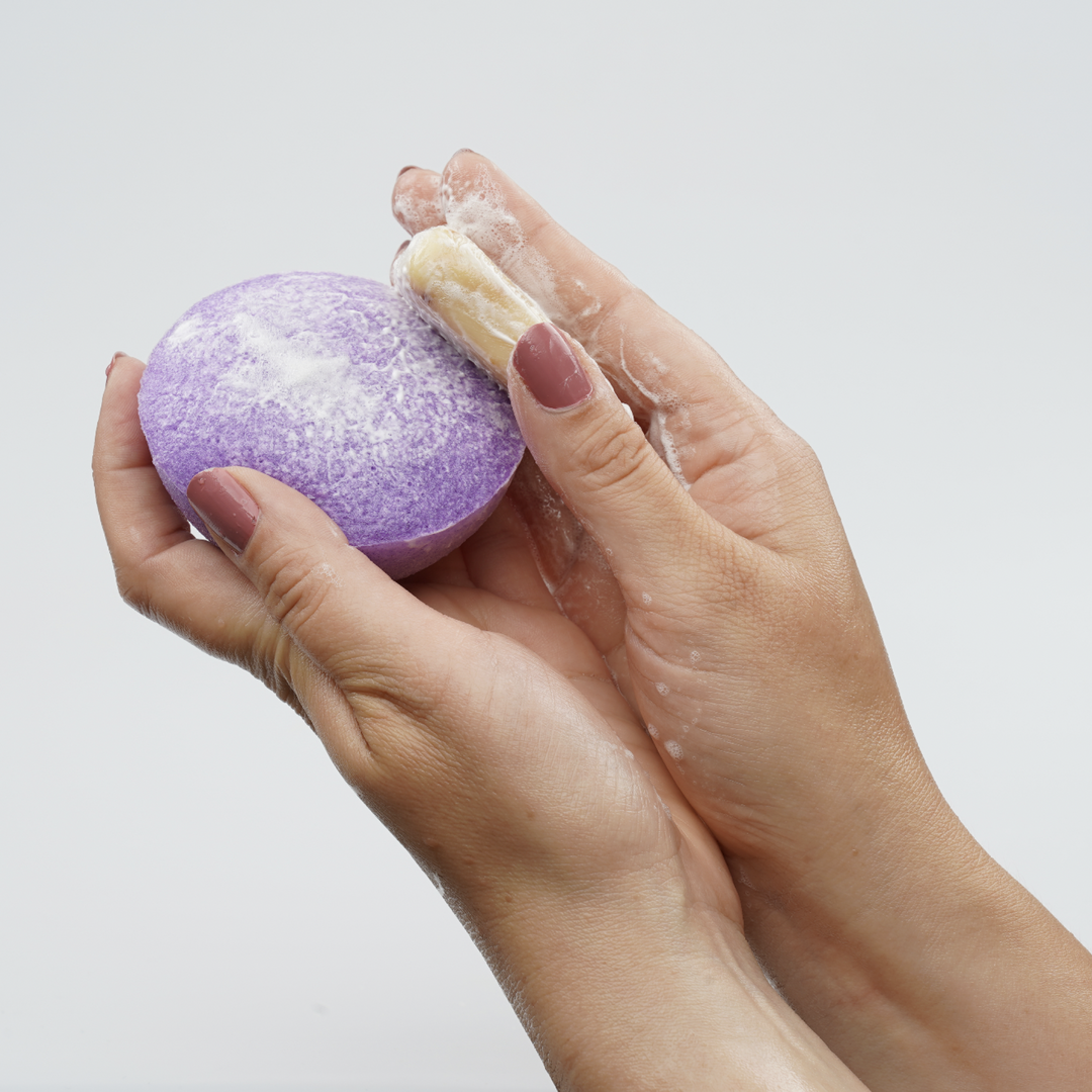 Purple facial cleansing sponge disc held in hands with light foam residue