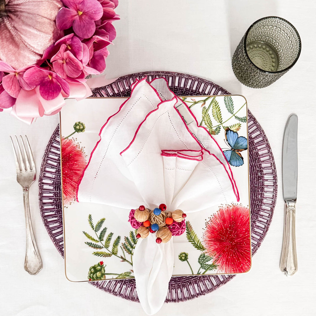 White linen napkin folded with pink ruffled hemstitch edges on a decorated plate