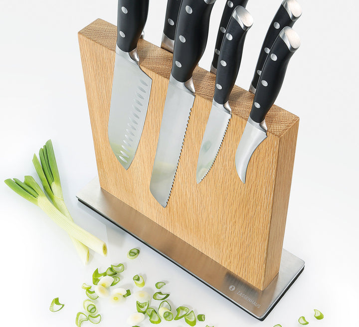 Light wood magnetic knife block with multiple knives in vertical slots, with chopped leeks