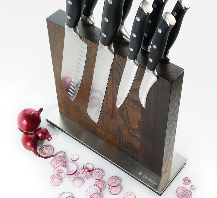 Wood magnetic knife block with several knives in slots, next to red onions