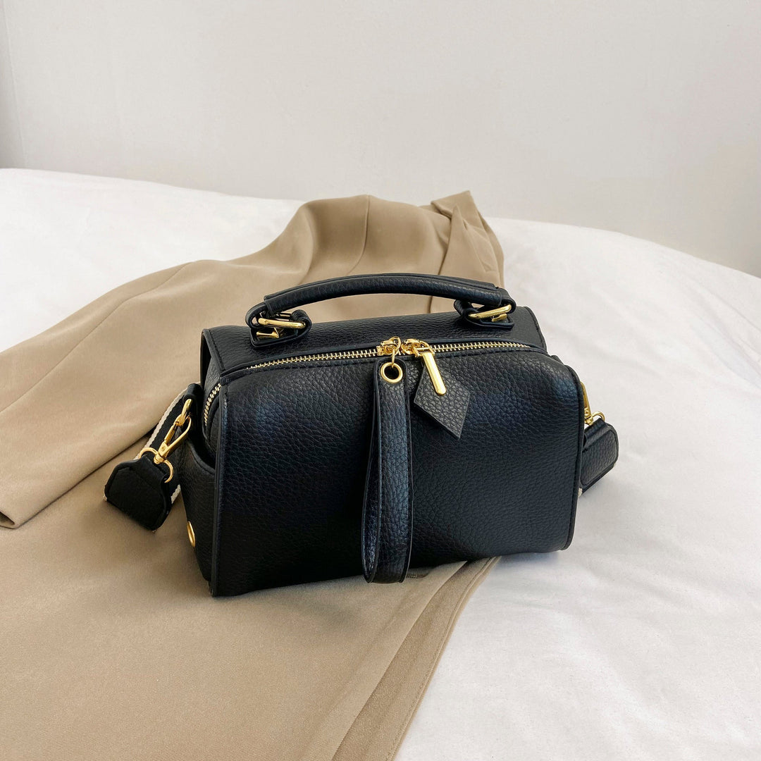 Black mini barrel bag with top handle, front strap panel, and gold-tone hardware