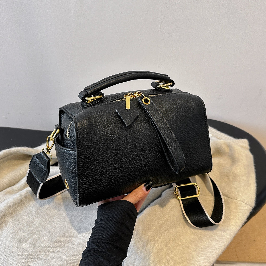 Black mini barrel bag with top handle, crossbody strap, and gold-tone hardware
