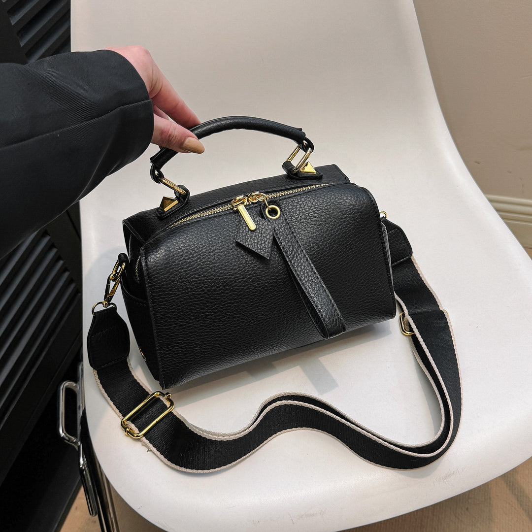 Black mini barrel bag with zipper top, crossbody strap, and gold-tone hardware