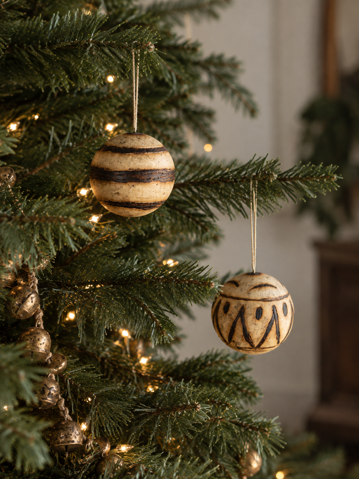 Marula fruit ornaments hanging among pine branches, round carved wooden baubles with stripe and dot designs