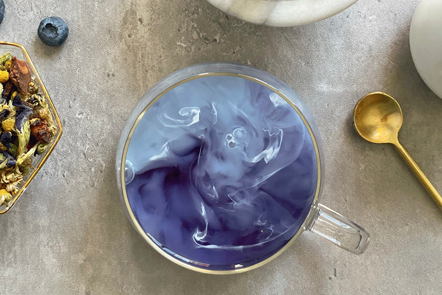 Glass mug of purple berry tea with visible tea leaves and steam
