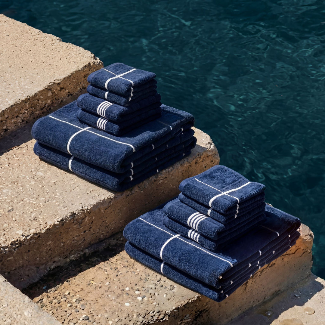 Stack of navy towels with white striped accents on a stone pool edge