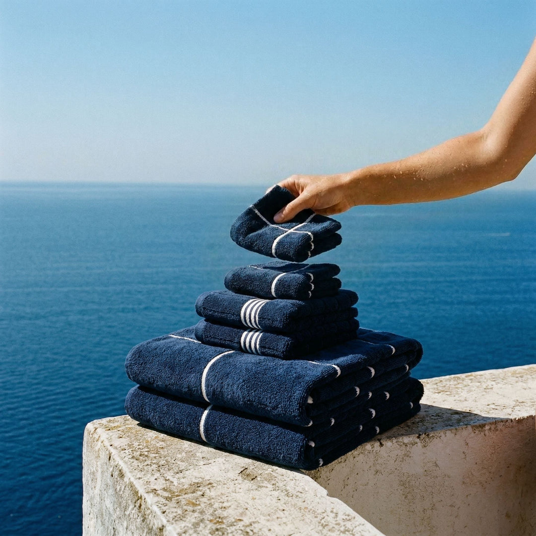 Person stacking navy towels with white stripe bands by the ocean