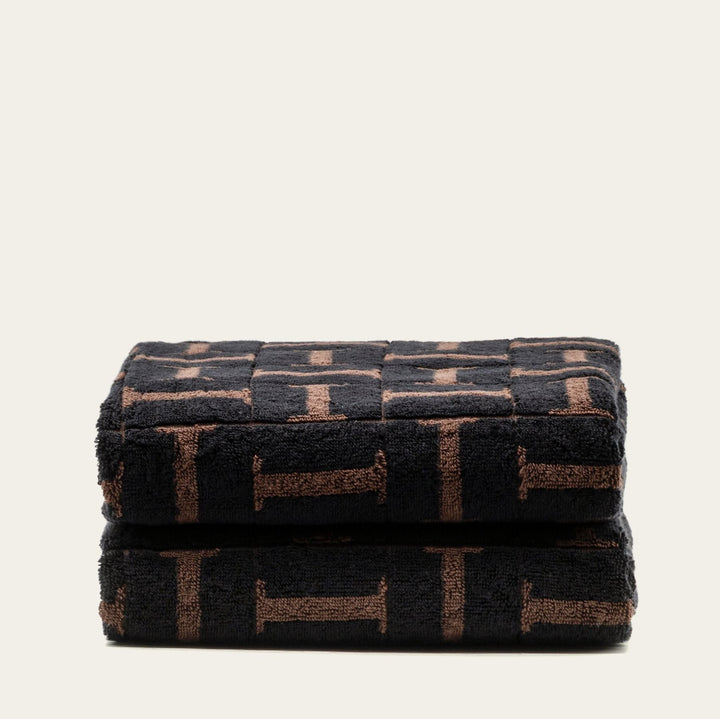 Folded bath towel with dark base and tobacco-brown block motif, stacked neatly.