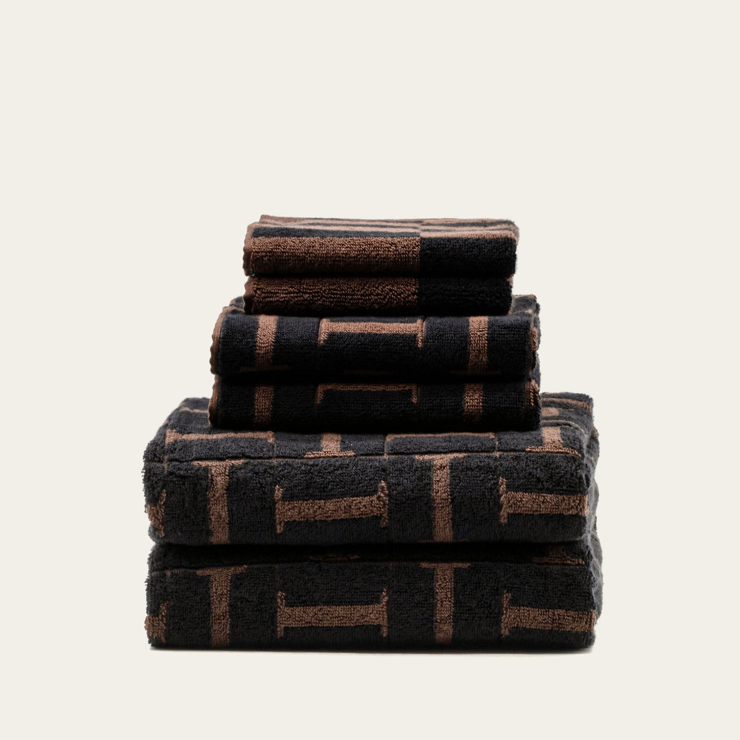 Stack of plush towels in dark tones with tobacco-brown geometric pattern blocks.