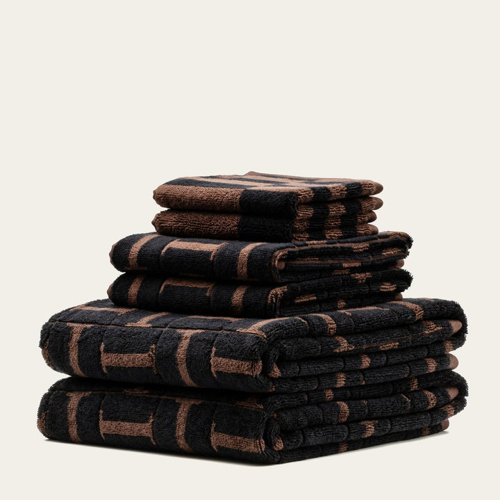 Neatly stacked towels showing dark geometric weave with tobacco-brown accents.