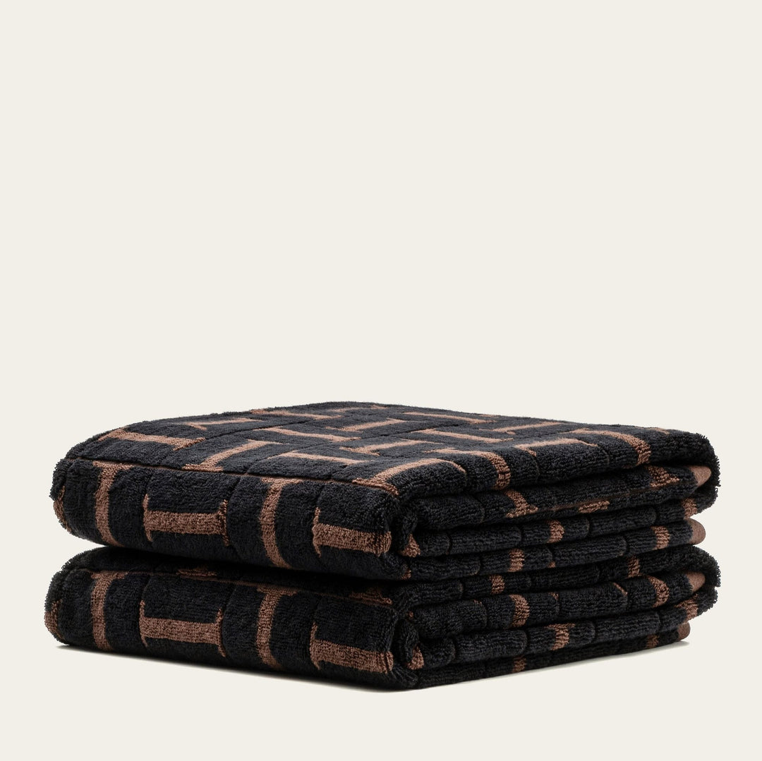 Two folded towels layered, dark base with tobacco-brown grid and stripe pattern.