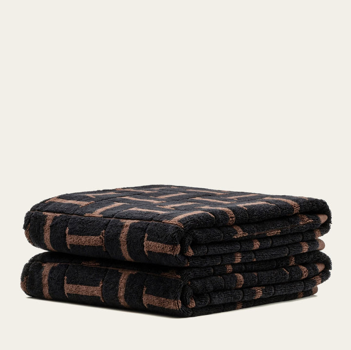 Two folded towels layered, dark base with tobacco-brown grid and stripe pattern.