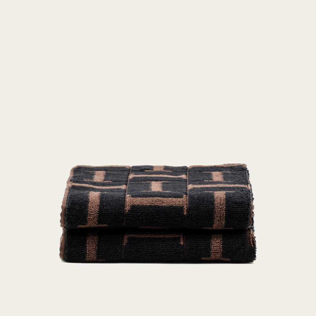 Rolled towel stack, dark base with tobacco-brown block pattern in plush cotton.