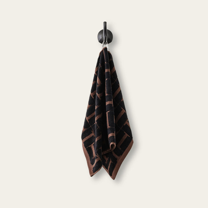 Hanging hand towel with dark fabric and tobacco-brown geometric weave detail.