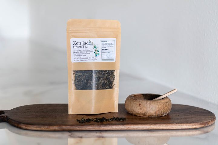 Resealable kraft pouch of loose green tea with wooden scoop on round tray