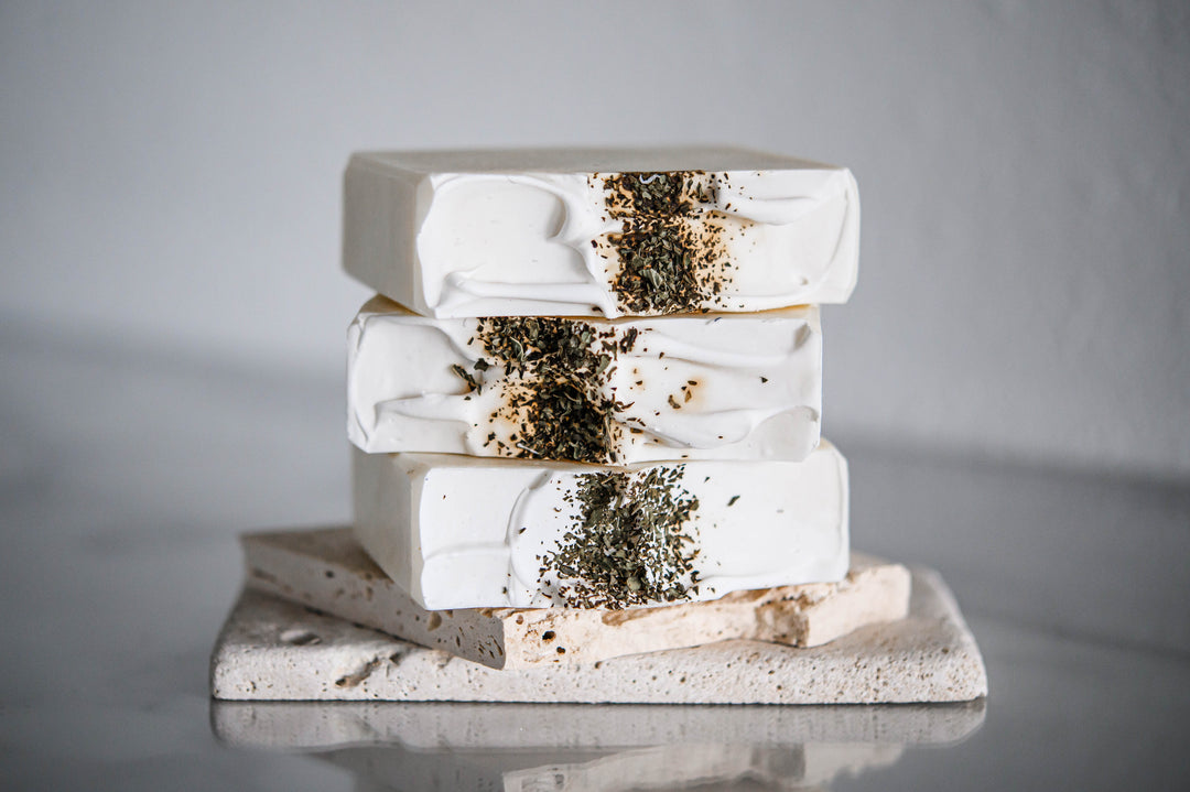 Stack of white handmade soap bars with green herb topping and molded ridges